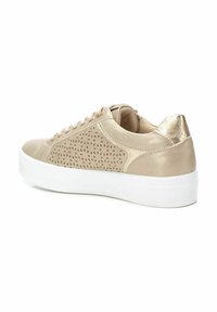 Zapatilla beige con diseño perforado, detalles metálicos y suela de plataforma blanca. Presenta cordones y una textura suave.