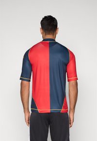 Czerwono-niebieska koszulka z krótkim rękawem i złotymi akcentami, z wzorem w dwóch kolorach. Wykonana z gładkiej, lekkiej tkaniny.