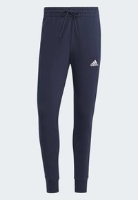 Temno modri trenirki iz mehke tkanine z vrvico za prilagajanje, zoženimi nogavicami in belim Adidasovim logotipom na levem stegnu.