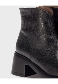 Botín negro de cuero con acabado texturizado, que cuenta con un resistente tacón cuadrado y un sutil logo de "wonders" en el lateral.