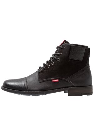 Bottes de cheville en cuir noir et en daim avec une pointe arrondie, un design à lacets, une étiquette logo rouge Levi's et un panneau arrière texturé.