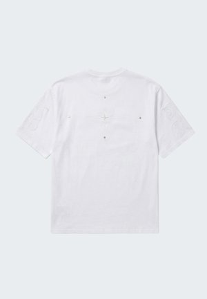 T-shirt blanc à manches courtes avec des motifs en relief subtil sur les manches et de petites clous métalliques disposés autour d'un dessin de croix centré dans le dos.