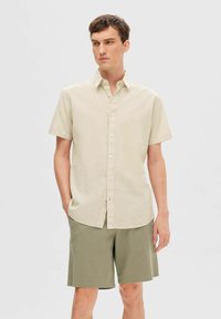 Kortsleeve skjorte i beige linblanding, med knappestolpe foran og klassisk krage, kombinert med olivengrønne shorts.
