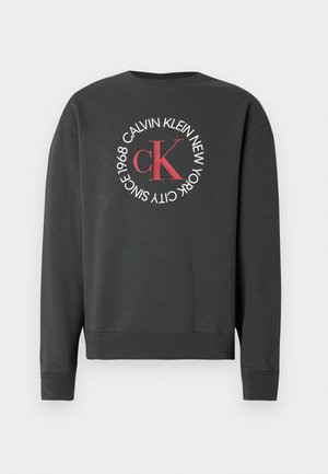 Sweatshirt cinzento escuro com um logótipo redondo que apresenta "Calvin Klein New York" e "Since 1968" em branco, com um "cK" vermelho no centro.