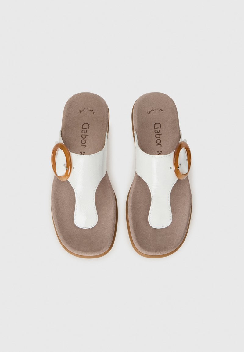 Witte slipper sandalen met een grote ronde gesp, tegen een effen achtergrond, met zachte inlegzolen zichtbaar aan de binnenkant.