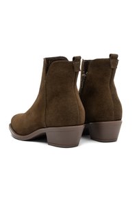 O pereche de cizme scurte din suedi maro, cu tocuri joase și fermoare pe lateral, văzute din spate pe un fundal alb.