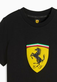Mustarin musta T-särk, millel on Ferrari logo: ratsutav hobune mustal kollasel kilbil, mille servad on roheline ja punane.