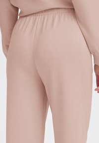 Helle rosa Jogginghosen mit elastischem Bund, glatter Textur und zulaufenden Beinen, die ein schlichtes und minimalistisches Design zeigen.