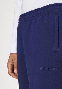 Mörkblå mjukisbyxor av mjukt tyg med elastisk midjeband och sidoficka; har präglad logotyp "Humanrace" på framsidan.