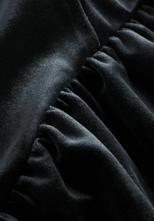 Černá látka se směsí hladkých a lehce texturovaných částí, s nařasenými záhyby, které vytvářejí hloubku a rozměr po celém materiálu.