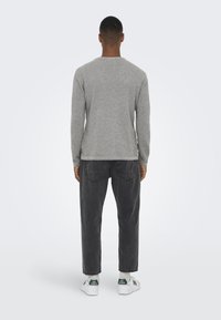 Camicia lunga grigia e texture con scollo rotondo, abbinata a pantaloni grigi scuri e sneakers bianche con accenti verdi.
