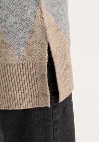 Stickad tröja med en beige, grå och krämfärgad blockdesign, med en texturerad ribbad nederkant och sidofickor för extra detalj.