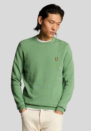 Maglione verde a maglia con scollo rotondo, caratterizzato da un piccolo emblema giallo sul petto. Texture morbida, polsini e orlo a costine.