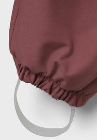 Sac à cordon élastique en tissu rose foncé avec une surface texturée et une sangle plate blanche, présentant des détails froncés à l'ouverture.