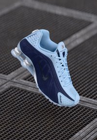 Blau und marineblaue Sportchuhe mit Netzgewebe, strukturierten Overlays und Gummisohle. Merkmale ein auffälliges Swoosh-Logo, Schnürdesign und Dämpfungselemente.
