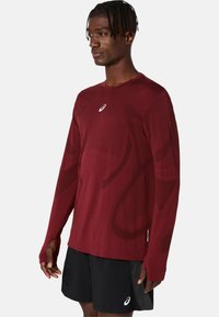 Langärmliges Sportshirt in Dunkelrot mit abstrakten Mustern, aus atmungsaktivem Stoff gefertigt. Mit Rundhalsausschnitt und Logo auf der Brust.
