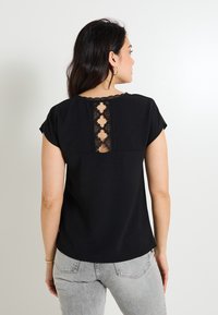 Top negro de manga corta con una tela texturizada, que presenta un diseño de espalda de encaje y un escote redondo. Combínalo con jeans gris claro.