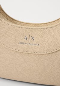 Borsa beige in pelle con una finitura liscia e una trama leggermente ruvida. Presenta un bordo cucito e un logo argentato con la scritta "A/X ARMANI EXCHANGE."