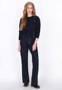 Marineblå striktrøje med struktureret stof, rund halsudskæring og fem sølvknapper. Parret med mørkeblå brede denimbukser og sorte sko.