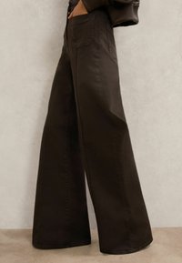 Široké hnedé nohavice z denimu s bočnými vreckami a hladkou textúrou, s vysokým pásom a čistým, jednoduchým šitím.