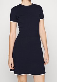 Robe tricotée bleu marine avec des manches courtes, une bordure blanche, un col rond, un bustier ajusté et un ourlet évasé, mettant en valeur une texture lisse et des accents côtelés.