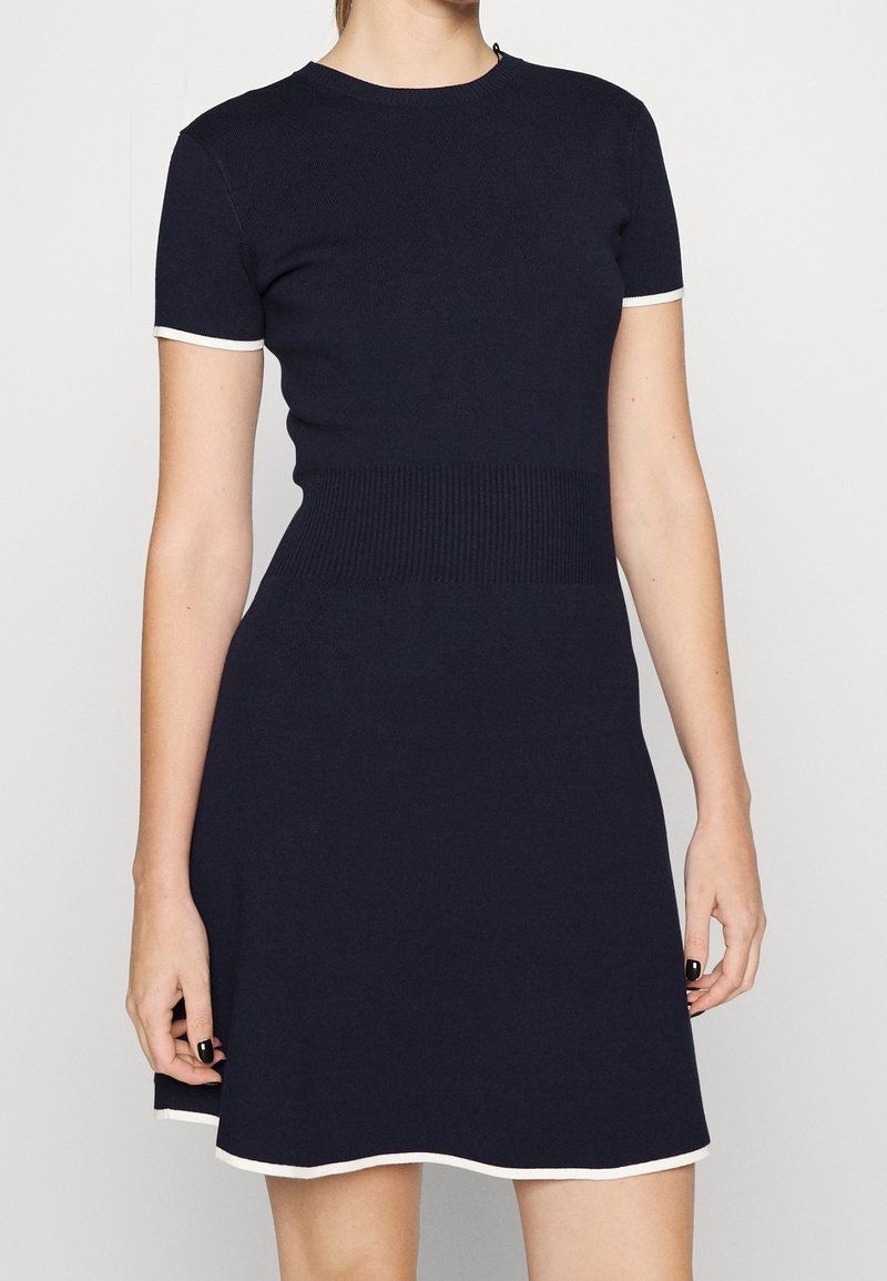 Robe tricotée bleu marine avec des manches courtes, une bordure blanche, un col rond, un bustier ajusté et un ourlet évasé, mettant en valeur une texture lisse et des accents côtelés.