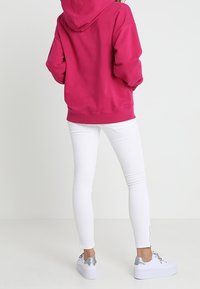 Felpa fucsia con cappuccio e polsini a coste, abbinata a jeans skinny bianchi. Presenta dettagli argentati su sneaker bianche con platform.