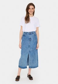 Farmer maxi szoknya elöl hasítékkal, magas derékkal és kék mosással. Fehér pólóval és barna loaferekkel párosítva. Sima textúra.