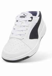 Sneaker blanche avec accents noirs, en cuir lisse, bout rond, tige perforée, design à lacets et semelle en caoutchouc. Avec logo Puma.