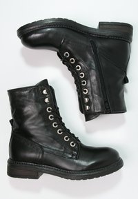 Bottes basses en cuir noir avec bout rond, devant à lacets, fermeture éclair latérale et détails en métal argenté. Texture avec un talon en bois plat.