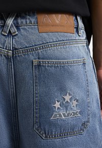 Szorty dżinsowe w jasnoniebieskim kolorze z widoczną skórzaną metką. Posiadają tylną kieszeń z białymi haftowanymi gwiazdkami i logo. Charakteryzują się wyraźnym detalem w postaci szwów.