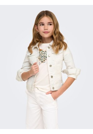 Mlada deklica z valovitimi blond lasmi, oblečena v belo denim jakno, bele hlače in majico z vzorcem leopardjega srca.