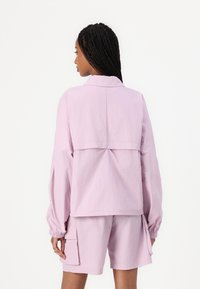 Lichtroze, lange mouwen jas met een kraag, voorzien van een geplooide achterpand en elastische manchetten, gecombineerd met bijpassende shorts met zijzakken.