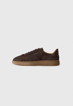 Brown suede sneaker with lace-up closure, tan rubber sole, and subtle branding on side. Features a streamlined silhouette and textured accents.