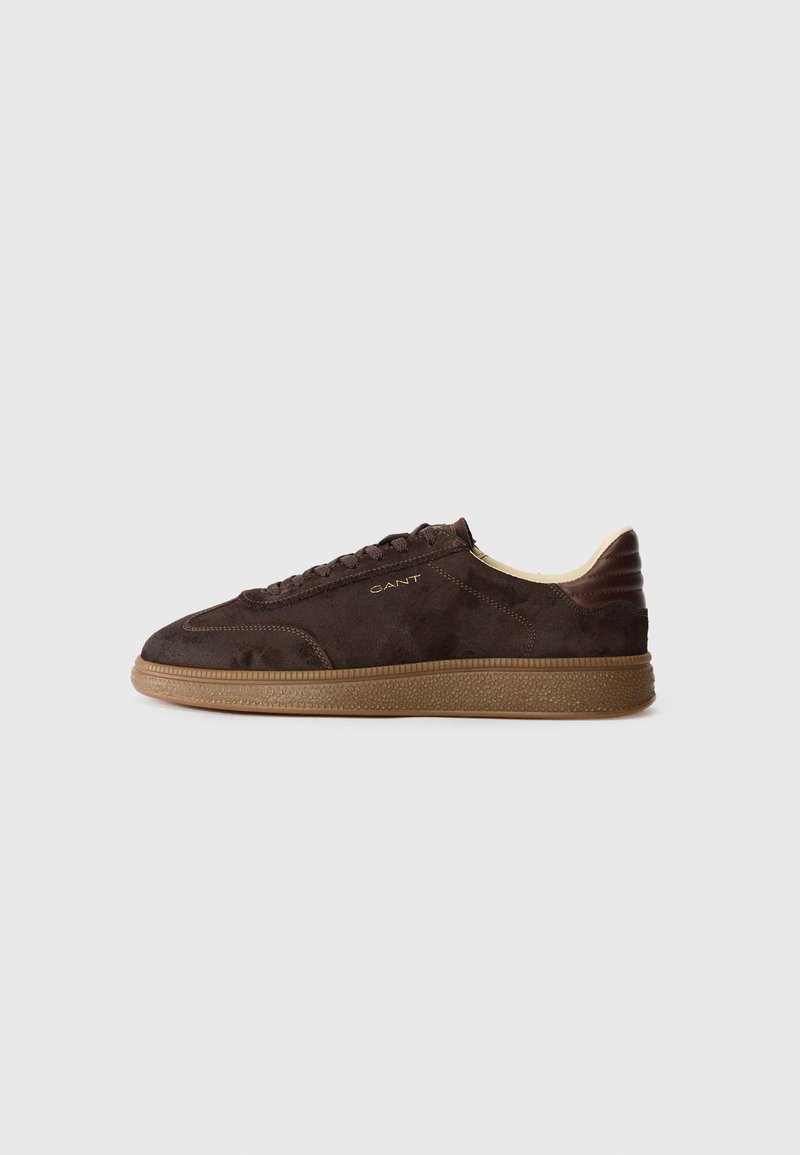 Brown suede sneaker with lace-up closure, tan rubber sole, and subtle branding on side. Features a streamlined silhouette and textured accents.