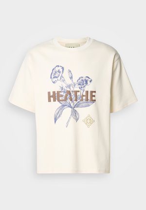 Cream cotton t-shirt featuring blue floral graphics and bold brown text "HEATHE." Loose fit with short sleeves and a crew neckline.
