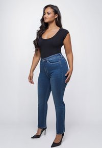 Zwarte body met een scoopneck, gecombineerd met hoge, blauwe jeans. De jeans hebben een klassiek ontwerp met zakken en een aansluitende pasvorm. Hoge hakken.