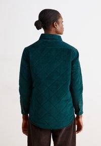 Chemise en velours côtelé teal avec texture en losange, manches longues, col et poignets à boutons, dotée d'un ourlet incurvé.