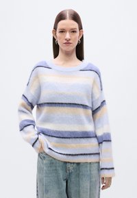 Pull rayé en matière douce et duveteuse. Présente des rayures bleu clair, crème et lavande avec des accents noirs. Col arrondi et coupe ample.