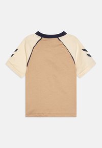 T-shirt med kort ärm, i beige kroppsfärg, krämfärgade ärmar och marinblå krage. Har mörkblå axelaccenter med sneda ränder. Tillverkad av mjukt bomullsmaterial.