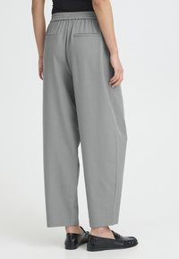 Grå vidde bukser med elastisk taljebånd og to baglommer. Stylet med sorte loafers, der viser en blød stoftekstur.