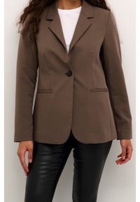 Blazer marron ajusté en tissu stretch, doté d'une fermeture à bouton unique, de revers crantés et de deux poches avant. Porté sur un haut blanc.