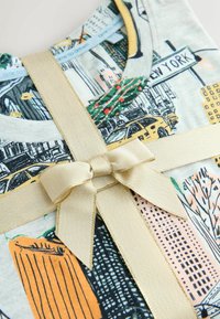 White cotton T-shirt features a New York cityscape print in black, yellow, and green, wrapped in gold ribbon with a bow.