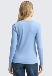 Hellblaues Langarmshirt mit rundem Halsausschnitt und strukturierter Stoffqualität. Hat ein tailliertes Design und dezente Nähte am Saum.
