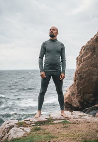 Szara termoaktywna bluzka i legginsy wykonane z teksturowanego, elastycznego materiału. Stojąc na skalistym brzegu, boso, na tle pochmurnego nieba i morza.