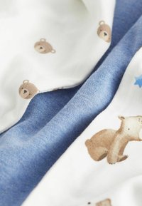 Baumwollstoff mit einem hellblauen Abschnitt und einem weißen Bereich, der mit kleinen Braunbären und Sternmustern gestaltet ist. Weiche Textur, verspieltes Design.