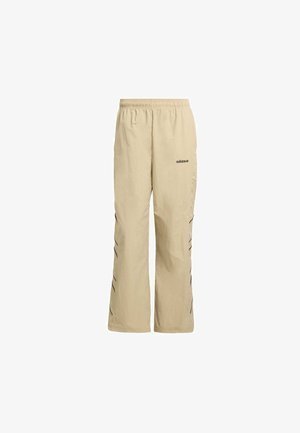 Pantaloni sportivi beige con vita elastica, vestibilità ampia, caratterizzati da accenti a zigzag neri lungo il lato e un logo Adidas stampato vicino all'anca.