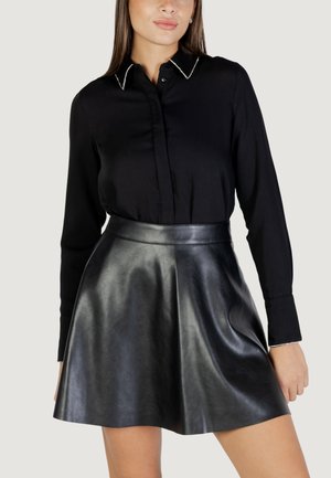 Camisa negra de botones con cuello puntiagudo y ribete blanco, combinada con una falda de cuero negra de cintura alta que se ensancha ligeramente en el dobladillo.