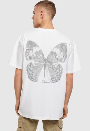 White cotton T-shirt featuring a large gray butterfly graphic on the back, with detailed line patterns and text "IDENTITY IS TRANSFORMATION."