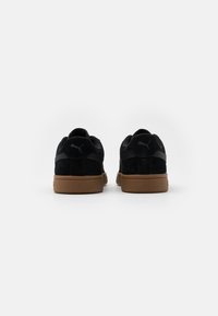 Sorte semskede sneakers med såle av brun gummi, med en strømlinjeformet design og subtil merkevareføring på hælen og sidene. Tekstura overflate.